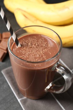 Cam bardakta lezzetli çikolatalı süt, siyah masada parçalar ve muzlar, yakın plan.