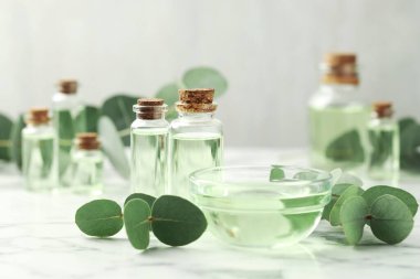 Yağ şişeleri, kase ve okaliptüs yaprakları beyaz mermer masanın üzerinde, yakın plan.