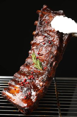 Siyah arka planda ızgaradan maşayla leziz domuz pirzolası alıp yakın plan çekiyoruz.