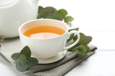 Fincanda romatik çay ve beyaz ahşap masada okaliptüs dalları, yakın plan.