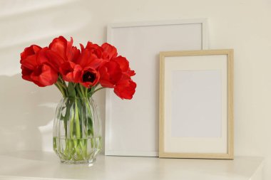 Güzel kırmızı laleler vazoda ve çerçeveler beyaz masada.