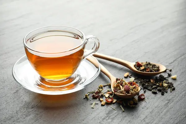 Lezzetli bitkisel çay ve kuru yapraklar siyah masada, yakın plan.