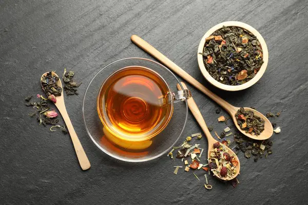 Lezzetli bitkisel çay ve kuru yapraklar siyah masada, düz yerde.