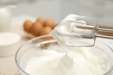 Masada çırpılmış krema ve çırpılmış kremayla el çırpıcı, yakın plan.