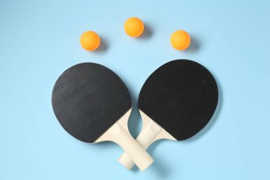 Masa tenisi raketleri ve topları açık mavi arka planda, düz yatıyordu.