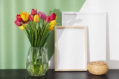 Renkli duvarın yanındaki masada bir buket güzel lale ve çerçeveler.