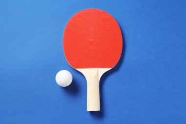 Mavi zemin üzerinde pinpon raketi ve top, üst görünüm