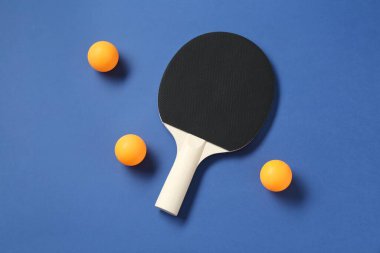 Masa tenisi raketi ve toplar mavi arkaplanda, üst görünümde.