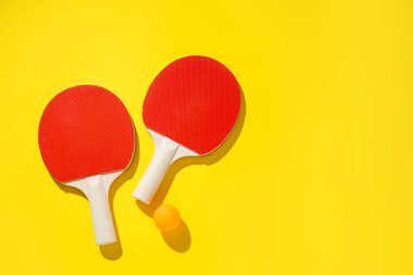 Masa tenisi raketleri ve top sarı arka planda, üst manzara. Metin için boşluk