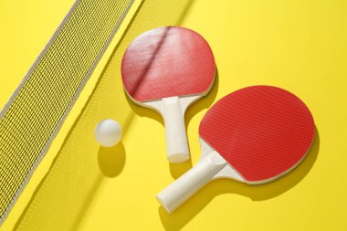 Sarı arka planda pinpon raketleri, top ve ağ.