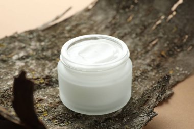 Bej arka planda vücut kremi ve ağaç kabuğu kavanozu, yakın plan.