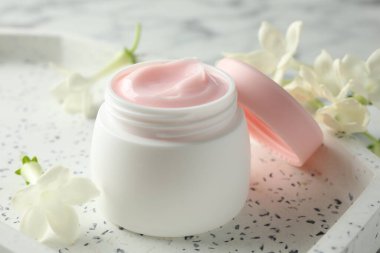 Beyaz masanın üzerinde bir kavanoz nemlendirici vücut kremi ve çiçekler, yakın plan.