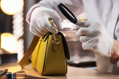 Kapalı bir masada deri çanta değerlendirmesi yapan büyüteçle bir eksper.