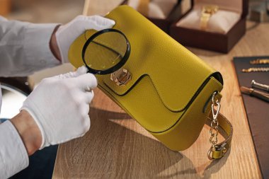 Kapalı bir masada deri çanta değerlendirmesi yapan büyüteçle bir eksper.