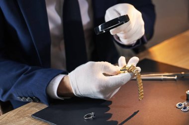 Büyüteci olan bir eksper. Masadaki lüks kol saatini değerlendiriyor. Yakın plan.