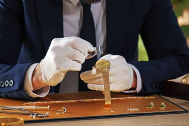 Loupe 'a değer biçen bir eksper. Masadaki lüks kol saatini değerlendiriyor. Yakın plan.