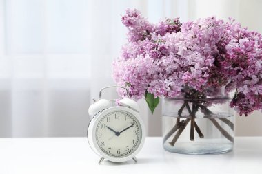 Cam vazoda güzel leylak çiçekleri ve kapalı masada çalar saat.