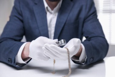 Beyaz masa içerisindeki lüks gerdanlığı değerlendiren eksper, yakın plan.