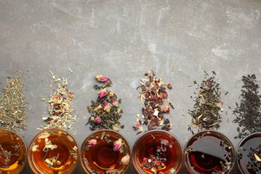 Cam fincanlarda aromatik bitki çayı, kuru yapraklar ve gri masada çiçekler, düz yatak. Metin için boşluk
