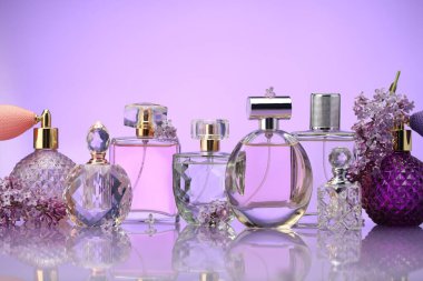 Ayna yüzeyinde mor arka planda parfüm şişeleri ve leylak çiçekleri