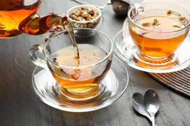 Siyah masada çaydanlıktan fincana bitkisel çay dökülüyor, yakın plan.