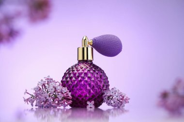 Bir şişe parfüm ve ayna yüzeyinde eflatun rengine karşı leylak çiçekleri, seçici odak