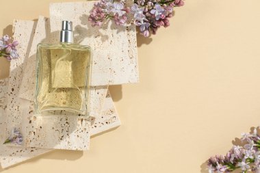 Bir şişe parfüm ve soluk sarı arka planda güzel leylak çiçekleri. Metin için boşluk