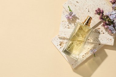 Bir şişe parfüm ve soluk sarı arka planda güzel leylak çiçekleri. Metin için boşluk