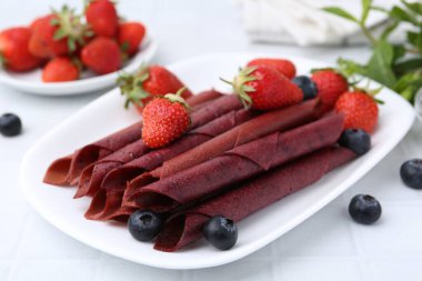 Lezzetli meyve dürümleri, çilekler ve yaban mersinleri beyaz masada, yakın plan.