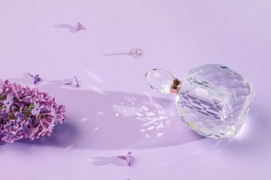 Bir şişe parfüm ve açık mor arka planda güzel leylak çiçekleri.