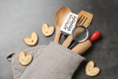 Fırın eldivenindeki farklı mutfak aletleri ve gri masadaki kurabiyeler.