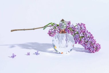 Parfüm şişesi ve dalında açık gri arka planda leylak çiçekleri, yakın plan.