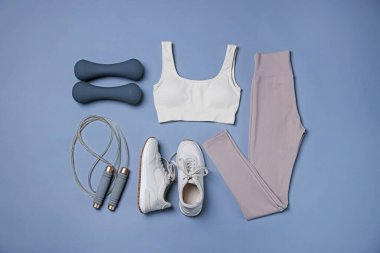 Spor kıyafetleri, spor ayakkabıları, ip atlama ve gri arka planda dambıllar, düz yatış.