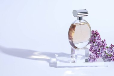 Parfüm şişesi ve açık gri arka planda leylak çiçekli dal, yakın plan. Metin için boşluk
