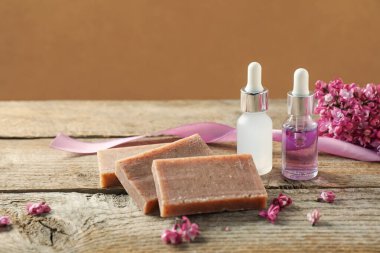 Sabun çubukları, esaslı yağ ve leylak çiçekleri ahşap masada kahverengi arka planda, yakın plan