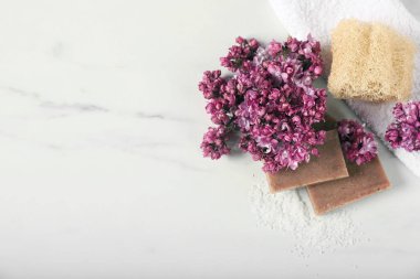 Sabun çubukları, deniz tuzu, lif süngeri ve beyaz mermer masa üzerinde leylak çiçekleri. Metin için boşluk