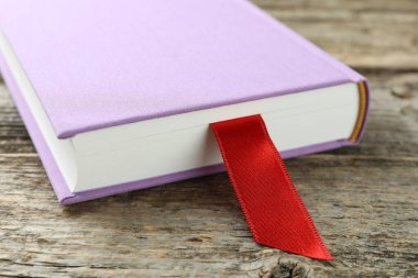 Ahşap masada kırmızı kurdele yer imi olan bir kitap, yakın plan.