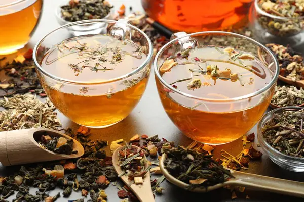 Aromatik bitki çayı ve kuru yapraklar gri masada, yakın plan.