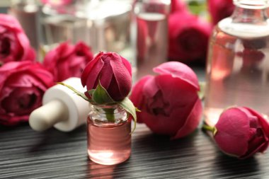 Aromatik esanslı parfüm şişelerini aç ve gri ahşap masada güller, yakın plan.