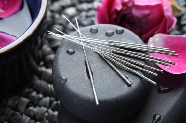 Akupunktur iğneleri, ıslak spa taşları ve hasır hasırın üzerindeki çiçekler, yakın plan.