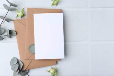 Boş tebrik kartı, kağıt zarflar, gül çiçekleri ve arka planda okaliptüs dalları, düz bir zemin. Metin için boşluk