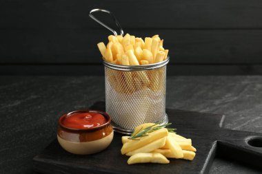 Lezzetli patates kızartması, ketçap ve biberiye ile servis ediliyor, siyah masada, yakın plan.