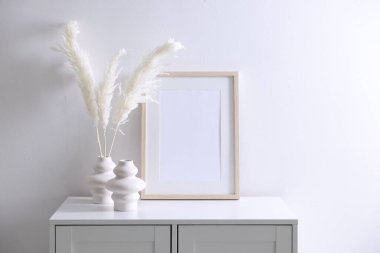 Beyaz duvarın yanındaki dolapta boş resim çerçevesi ve şık ev dekorasyonu