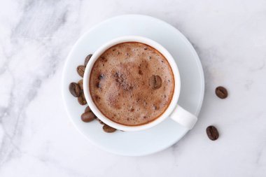 Kahve fincanda, fasulye ve çay tabağı beyaz mermer masada.