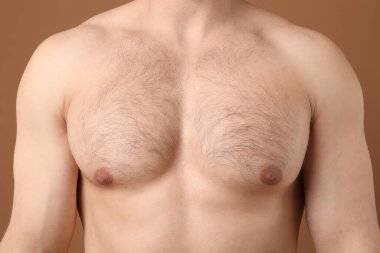 Kıllı göğüslü, kahverengi arka planda genç bir adam, yakın plan. Epilasyon işlemi