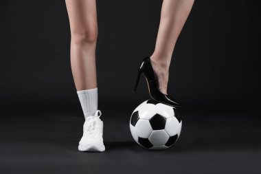 Arka planda futbol topu olan yüksek topuklu ayakkabılı ve spor ayakkabılı bir kadın.