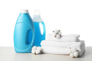 Kumaş yumuşatıcı şişeler, pamuk çiçekler ve beyaz arka plana karşı ahşap masa üzerindeki havlular.