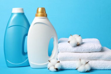 Yumuşatıcı şişeler, pamuk çiçekleri ve açık mavi arka planda havlular.