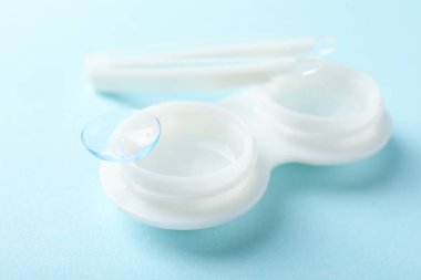 Açık mavi arkaplanda kontak lensler, bavul ve cımbızlar, yakın plan