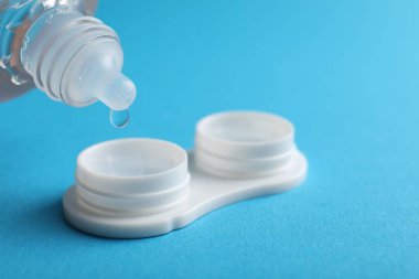 Açık mavi arka planda kontakt lensleri olan çözeltiye damlatılıyor, yakın plan. Metin için boşluk